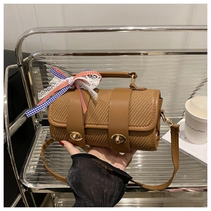 Close-up of brown cylindrical woven crossbody bag with dual gold locks and plaid bow