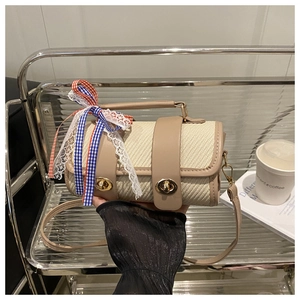 Close-up of beige woven cylinder handbag with leather straps and a colorful ribbon bow