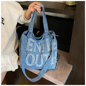 Detail of blue denim tote bag featuring frayed edge Gentle Outh embroidery and large capacity