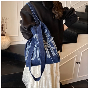 Detail of frayed letter patch on deep blue denim tote bag with long shoulder strap