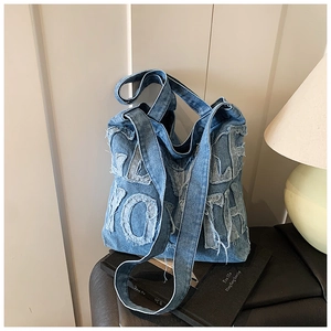 Detail of blue denim tote bag with vintage frayed letter patches on a leather stool