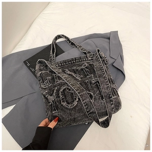 Close-up of distressed dark grey denim tote bag with frayed letter patches and texture