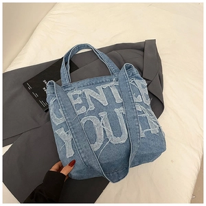 Close-up of vintage blue denim tote bag with frayed letter patchwork and wide strap
