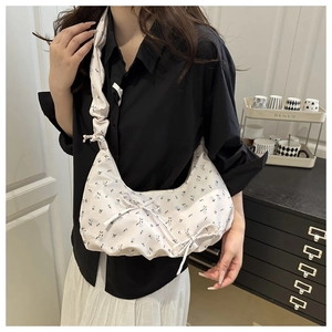 Detail of white floral crossbody bag with blue patterns, bow decor, and scrunchie strap