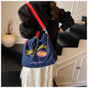 Detail of blue denim crossbody bag with yellow embroidery and red shoulder strap