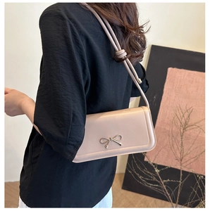 Detail of nude pink bow shoulder bag showing texture and golden butterfly metallic accent