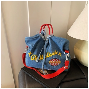Detail of blue denim bucket bag with Chibi vibes embroidery and red woven handle