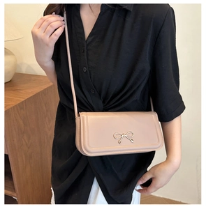 Detail of light beige baguette bag with golden bow buckle on a lifestyle model