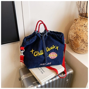Detail der blauen Denim-Tasche mit gelber Stickerei und rotem Schultergurt