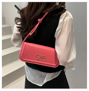 Detail of a bright pink baguette bag featuring a gold bow buckle and knotted leather strap