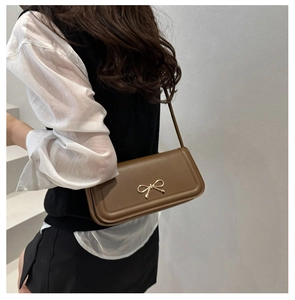 Side view of a vintage brown leather crossbody bag with a golden bow buckle on a model