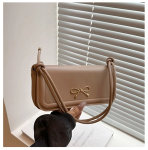 Detail of khaki leather handbag featuring a gold bow accent and tied knot strap detail