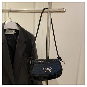 Close-up of black crocodile pattern shoulder bag featuring a gold metal bow clasp detail