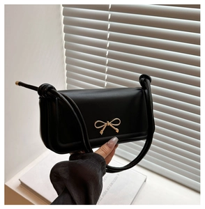 Close-up of black matte leather baguette bag with golden bow clasp and knotted strap detail