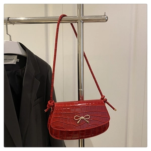 Detail of red crocodile texture handbag featuring an elegant metal bow clasp decoration