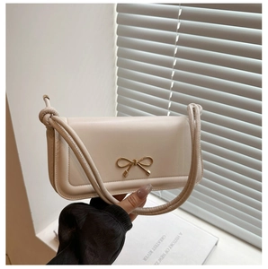 Detail of cream-white baguette bag featuring a gold bow buckle and knotted leather strap