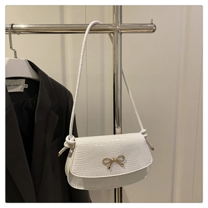 Detail of white crocodile texture handbag with a golden bow buckle on a metal stand
