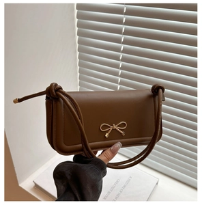 Detail of caramel brown leather handbag featuring a golden bow buckle and knotted strap