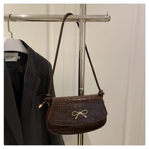 Detail of dark brown crocodile texture handbag with elegant gold bow metal clasp