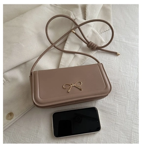 Detail view of tan leather baguette bag with gold bow buckle and slim shoulder strap