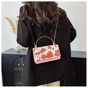 Vista trasera de bolso bandolera con estampado de vaca y asa dorada sobre blazer negro