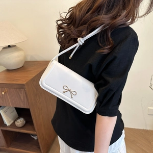 White minimalist baguette shoulder bag with gold bow clasp on a female model