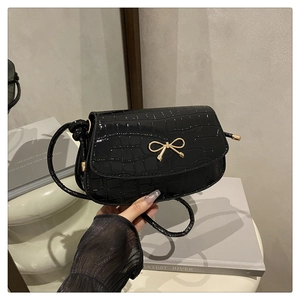 Detail of black crocodile texture bag with gold bow clasp and elegant glossy finish