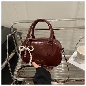 Detail of burgundy patent leather handbag with pearl bow charm and logo on glass shelf