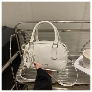 Detail of white glossy leather handbag with pearl bow charm on a modern display