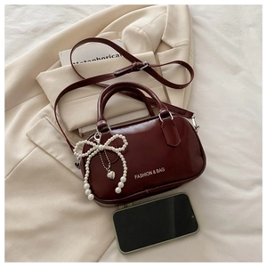 Detail view of burgundy vintage oil wax leather crossbody bag with pearl bow charm