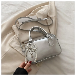 Close-up of silver crossbody bag with pearl bow charm and embossed BAGS text detail