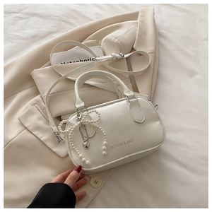 Detail of white leather handbag with pearl bow charm and heart pendant on a beige blazer