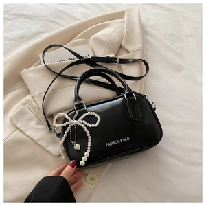 Detail of black glossy handbag with white pearl bow charm and silver heart pendant