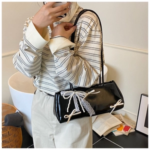 Detail of black glossy bag featuring delicate white lace bows and elegant pearl accents