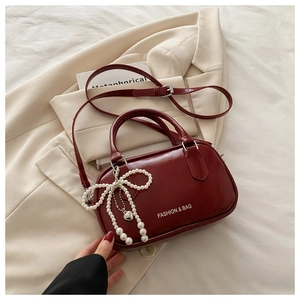Detail of burgundy leather handbag with pearl bow pendant and crossbody strap