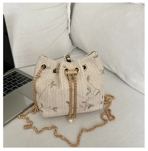 Close-up of woven bucket bag with floral embroidery, gold chain, and pearl drawstring