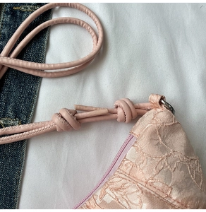 Close-up of pink lace shoulder bag with intricate hollow embroidery and knotted cord strap
