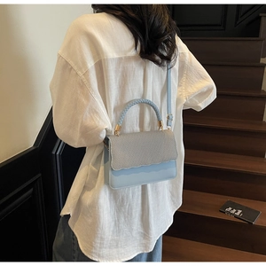 Close-up of light blue bag featuring a textured woven flap and elegant scalloped edges