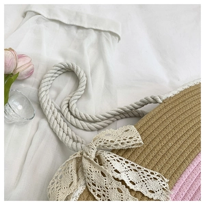 Detail of woven straw tote bag featuring a large white lace bow and thick cotton rope handles