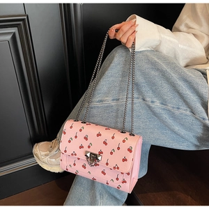 Sac bandoulière rose à motif cerises avec chaîne en métal porté par un mannequin