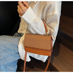 Detail of brown woven textured flap bag with wave edge on casual white shirt