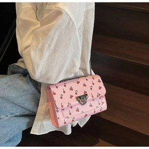 Sac bandoulière rose à imprimé cerise avec fermoir argenté porté par un mannequin
