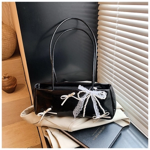 Close-up of black glossy pillow bag with white bows and pearl lace charm detail