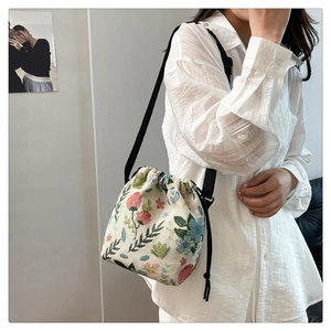 Floral embroidered bucket bag with drawstring closure and adjustable black strap on model