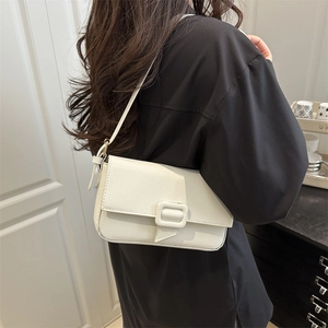Minimalist beige pebble leather crossbody bag with square buckle shown on shoulder