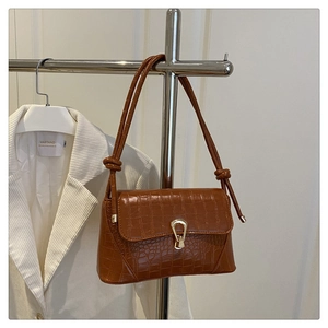 Detail view of the caramel crocodile pattern leather bag with a gold buckle and knotted strap
