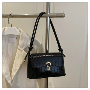 Detail of black crocodile pattern crossbody bag with gold teardrop clasp on white blazer