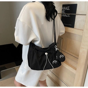 Detail of black nylon drawstring crossbody bag with round coin purse and white logo text