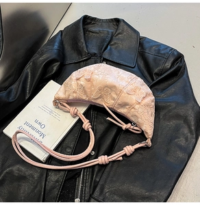 Detail of pink lace croissant bag with 3D butterfly embroidery on a dark background