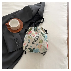 Detailed embroidery of colorful flowers on a cream canvas drawstring bucket bag